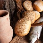 Vintage still life of an old wine jug with bread loaves and fresh fish